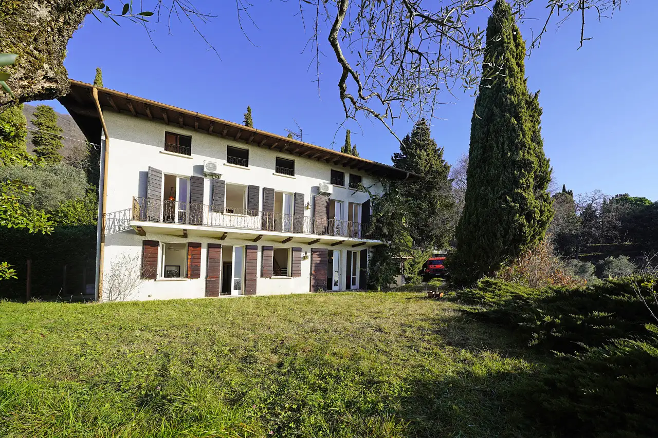 Villa-Fassade mit Garten und Bäumen unter blauem Himmel
