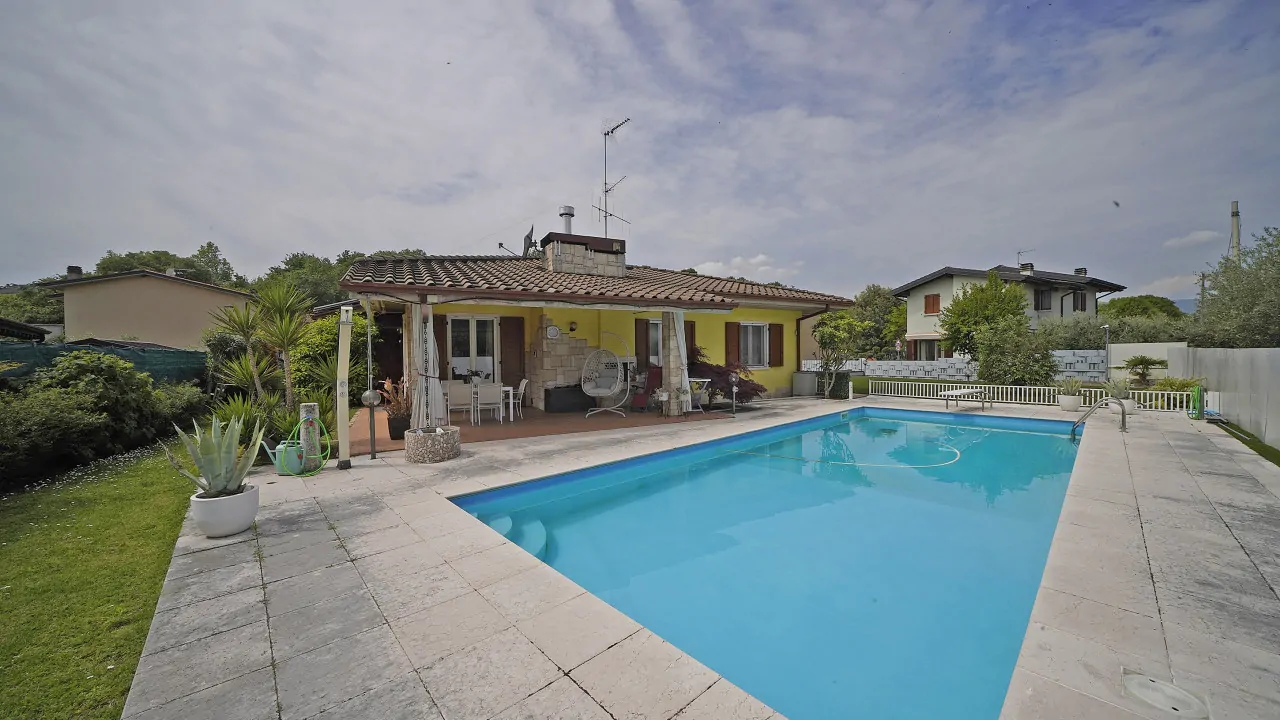 Rechteckiger Pool mit Steinrand vor Villa mit Veranda