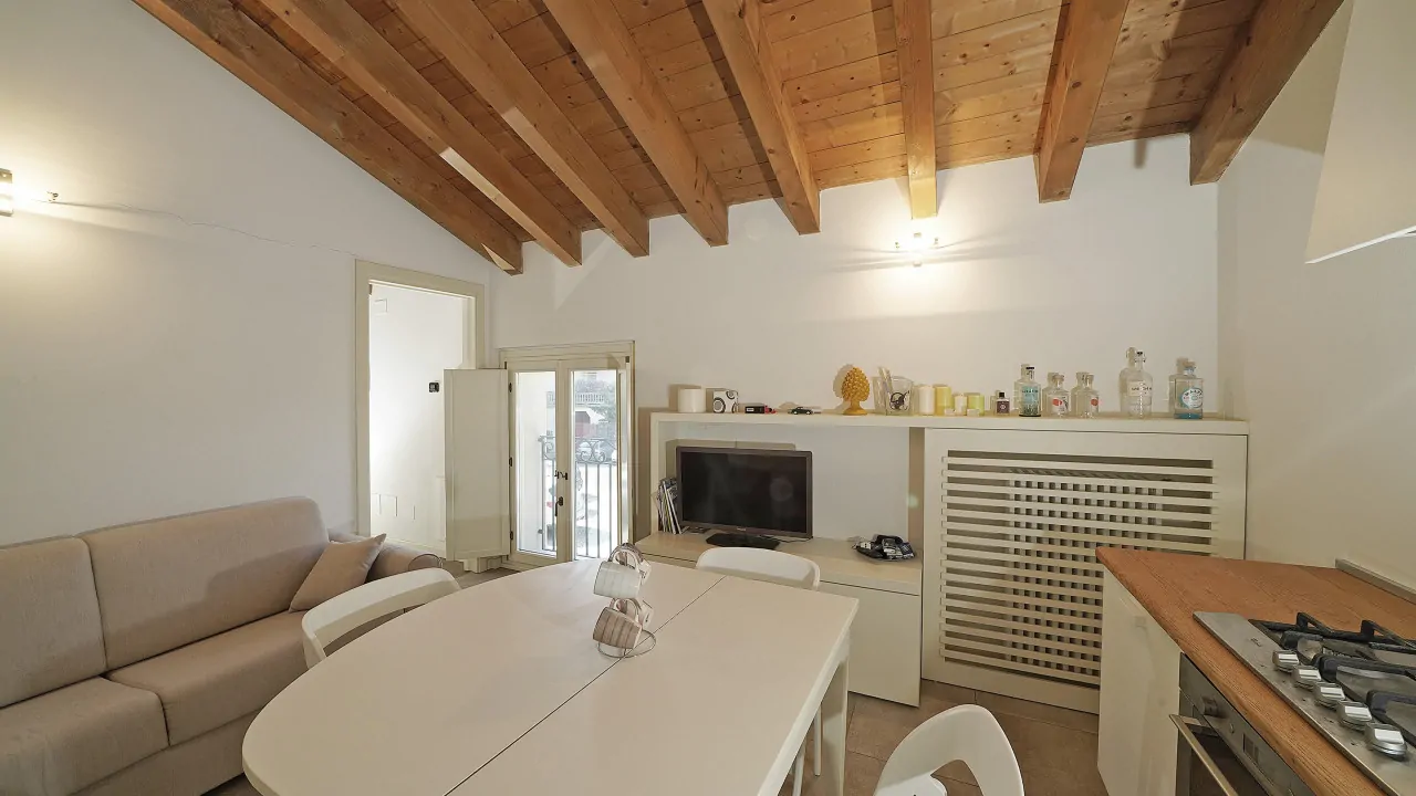 Soggiorno con tavolo bianco, divano beige e soffitto con travi in legno