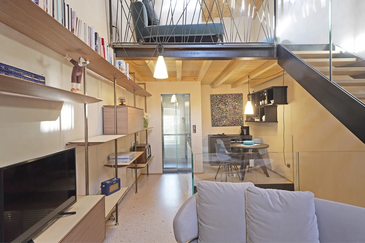 Soggiorno con divano, libreria e scala interna in metallo e legno