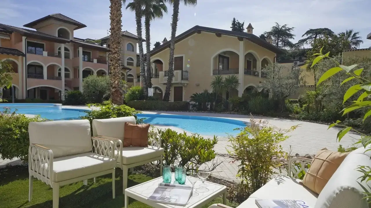 Zona piscina con sedute e tavolino nel giardino del residence