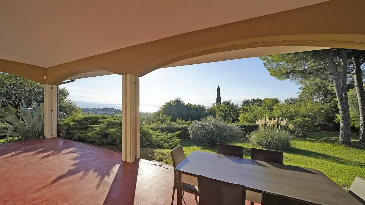 Terrazza coperta con tavolo e sedie e vista su giardino e lago