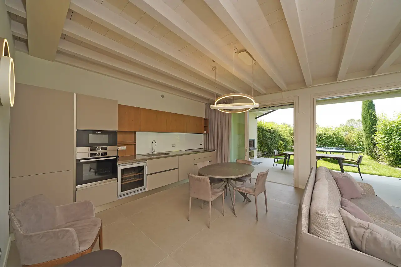 Living room with linear kitchen and round table near glass door to garden