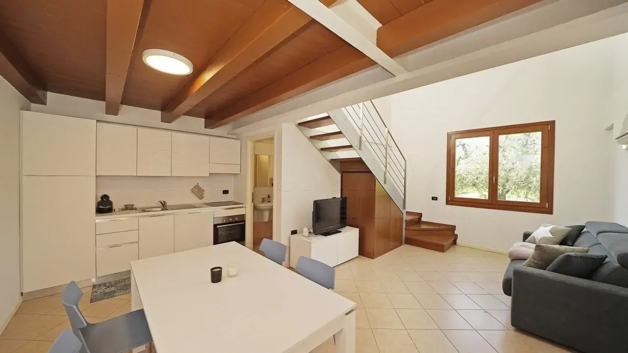 Wohnzimmer mit offener Küche, Tisch und Sofa unter Holzbalkendecke