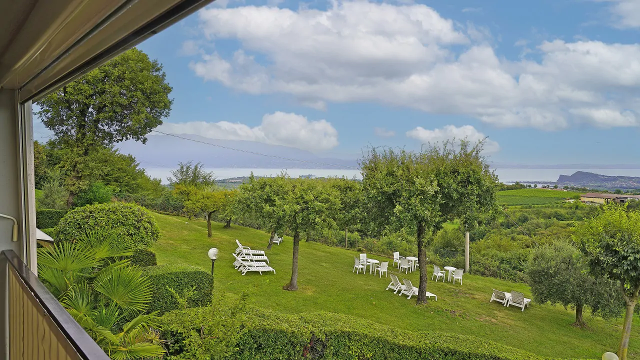 View from balcony over garden with trees and white chairs