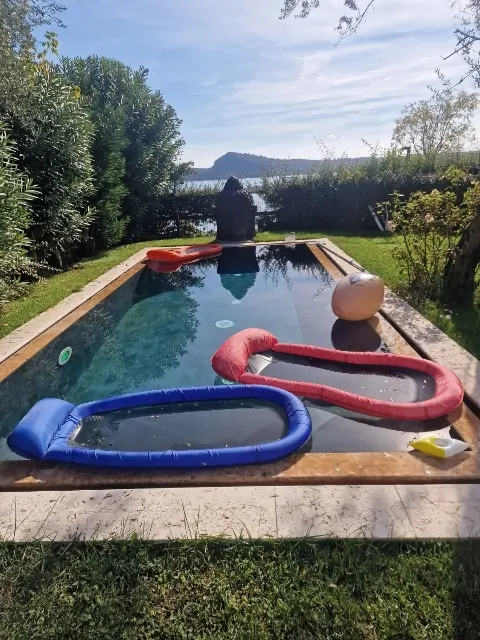Rechteckiger Pool mit aufblasbarem Spielzeug und Seeblick im Hintergrund