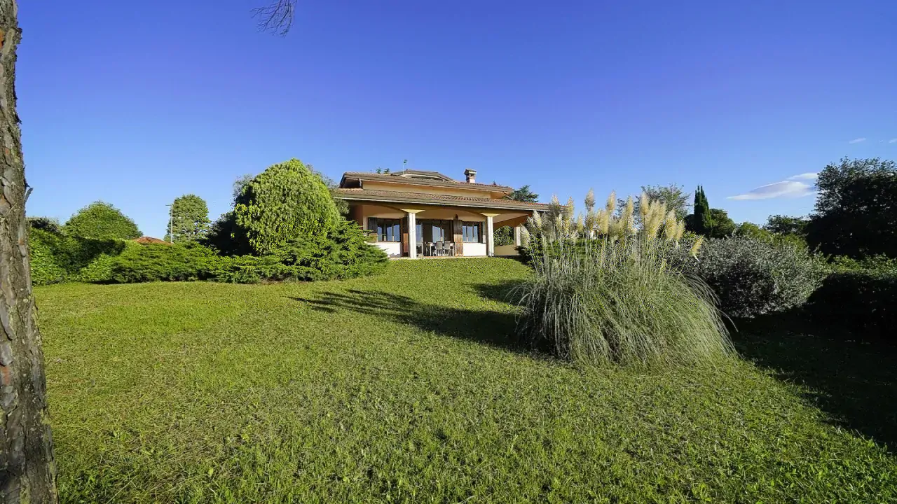 Large garden with lawn and bushes in front of detached villa