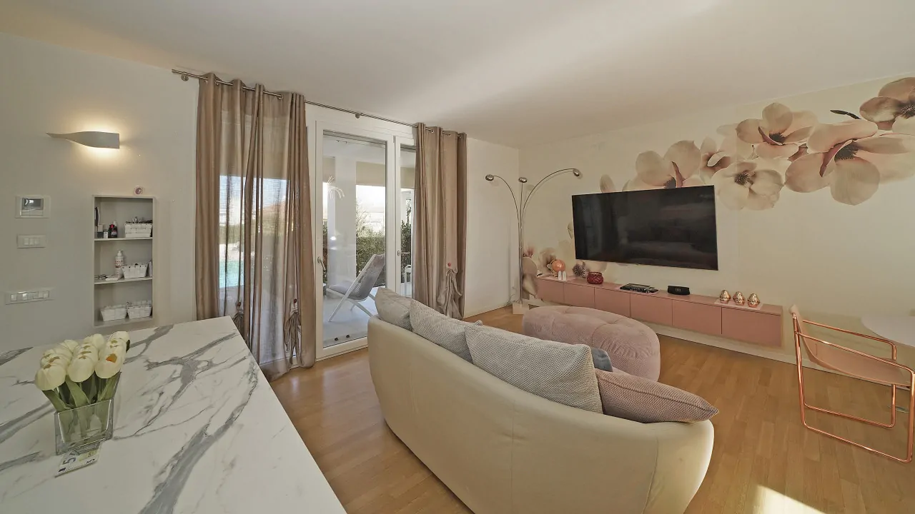 Wohnzimmer mit Sofa, TV-Schrank und Glastür mit Vorhängen