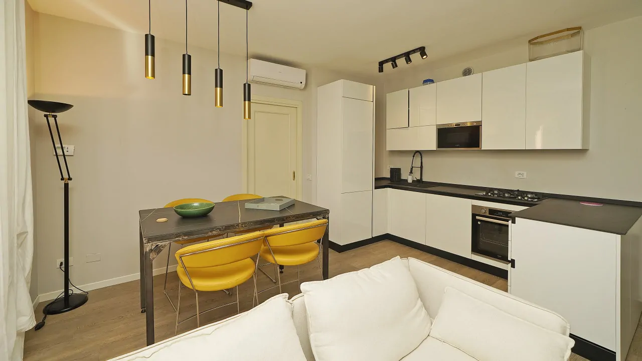 Wohnzimmer mit weißem Sofa, Tisch mit gelben Stühlen und moderner offener Küche