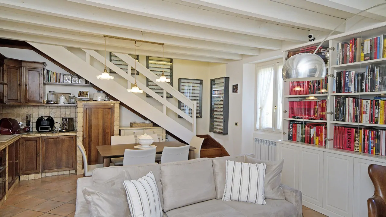 Wohnzimmer mit Sofa, Bücherregal und weißer Holztreppe