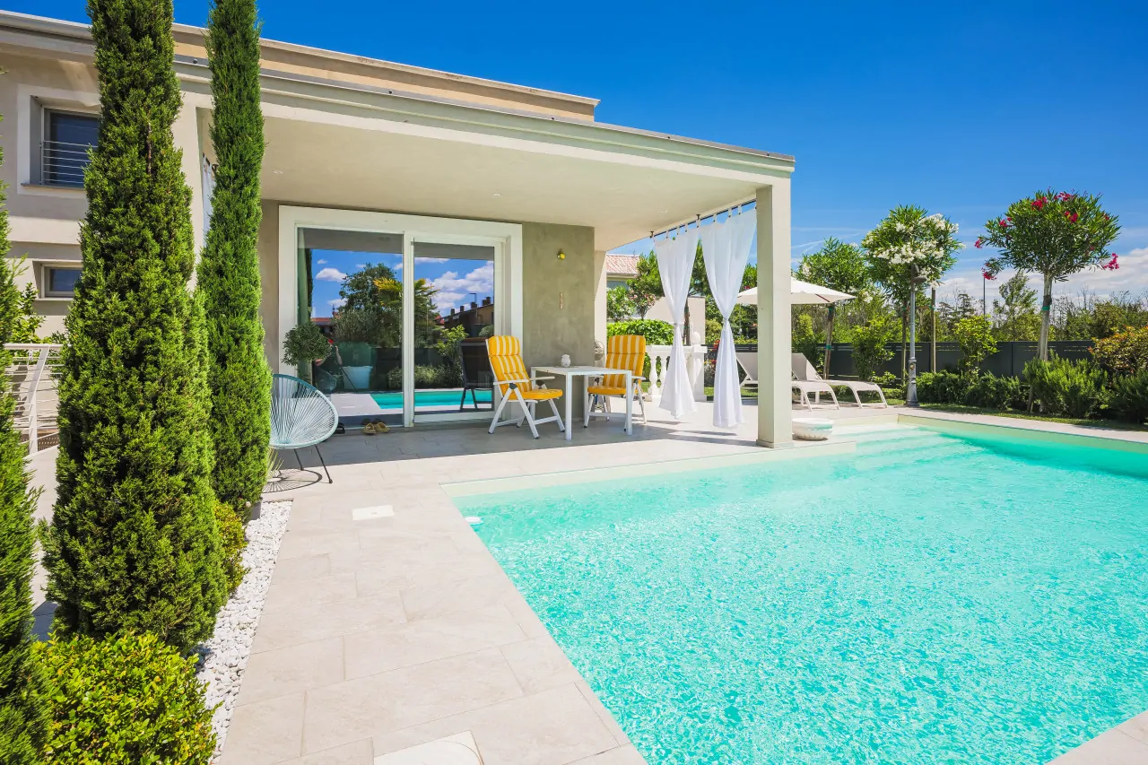 Swimming pool with tiled edge and covered veranda with chairs and white curtains