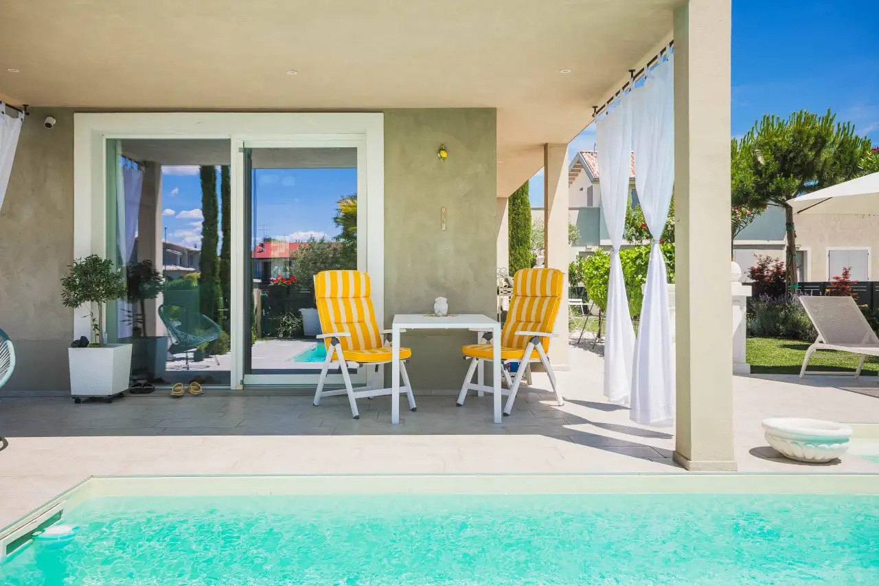 Swimming pool with edge and covered veranda with yellow and white striped deck chairs