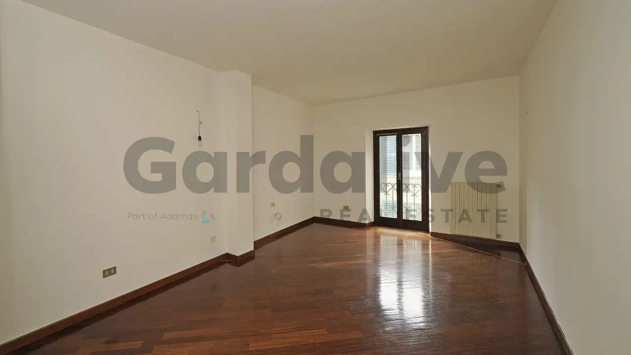 Soggiorno vuoto con pavimento in legno e porta finestra con ringhiera