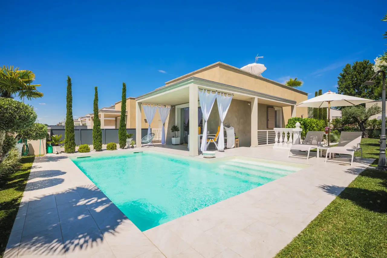 Piscina con bordo in pietra e pergolato con tende bianche