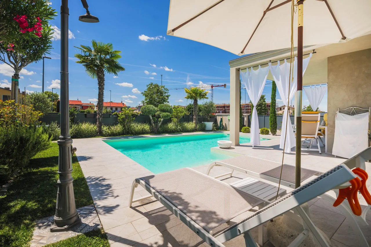 Piscina con lettini prendisole e ombrellone in giardino