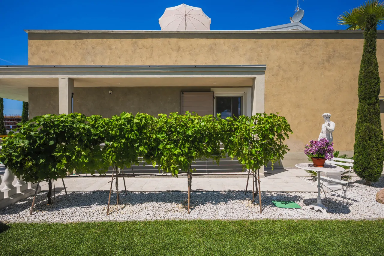 Giardino con siepe e statua bianca vicino a tavolo e sedia in ferro battuto
